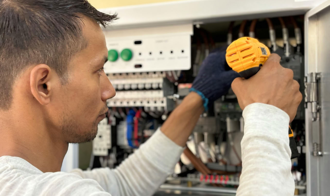 Focused technician using a drill on an electrical panel, showcasing expert workmanship.