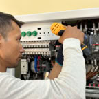 Professional electrician using a drill on an indoor circuit breaker panel.